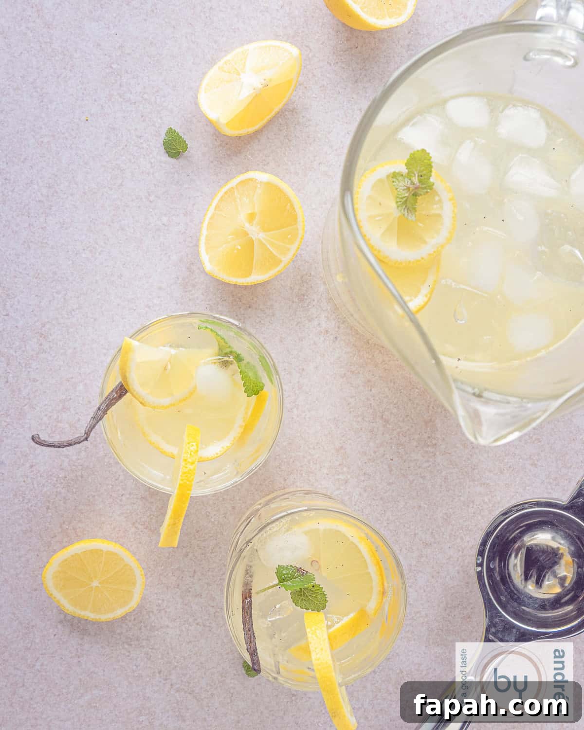 Vanilla Lemonade Recipe: Refreshing Homemade Citrus Cooler 8 A height photo topdown. Two glasses with vanilla lemonade, lemon and mint and a jar. Some lemon parts scattered around.