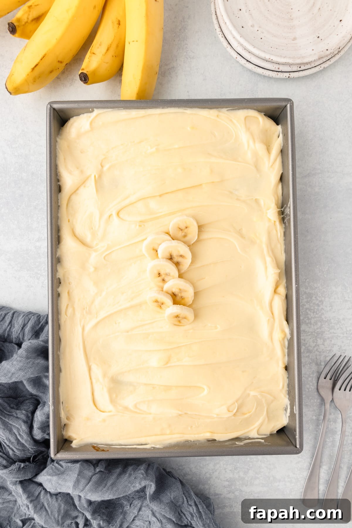 A banana cake made in a 9X13 cake pan, frosted with cream cheese frosting topped with 5 sliced banana pieces.
