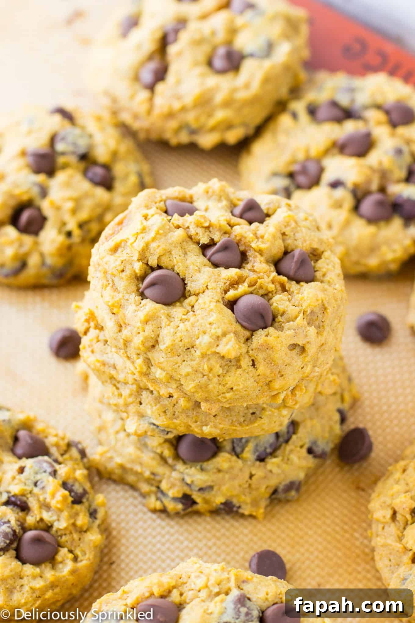 Chewy Pumpkin Oatmeal Cookies with Warm Spices 2 A stack of pumpkin oatmeal cookies with chocolate chips on the baking tray with more in the background.