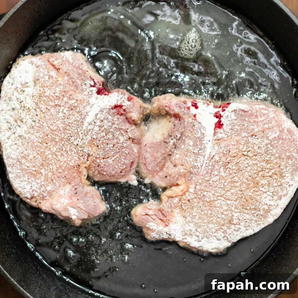 flour dredged pork chops frying in a cast iron skillet