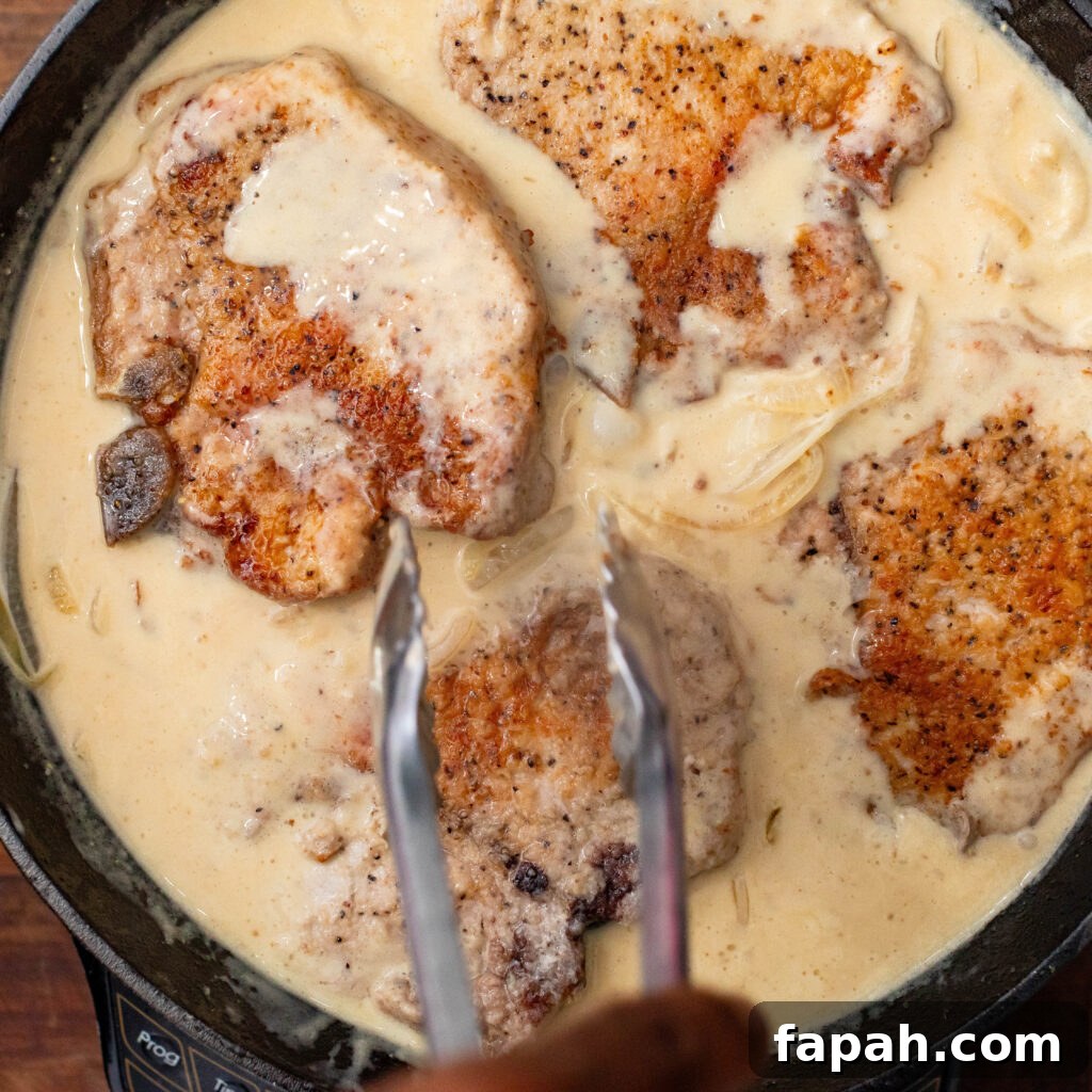 adding pork chops to cast iron skillet with gravy and onions
