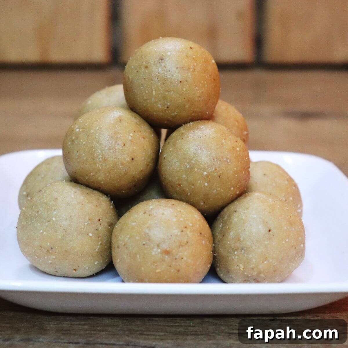 Peanut ladoos placed on a white plate on a brown counter top.