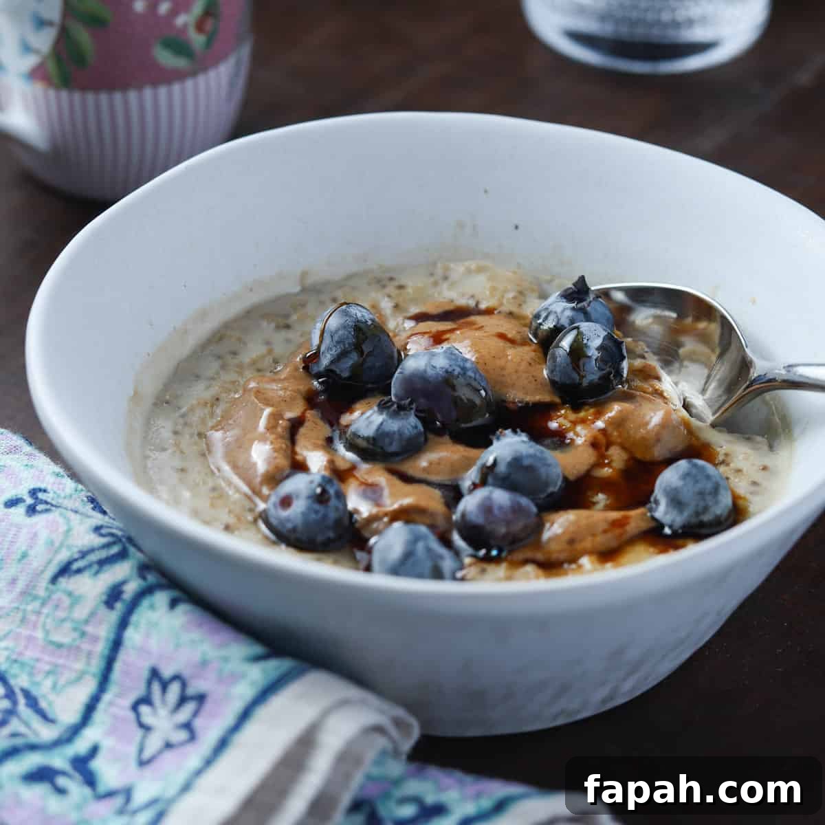 photo of a white bowl of vegan oat and chia seed porridge with blueberries and coconut almond butter on top.
