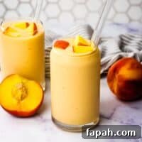Two banana peach smoothies garnished with chopped peaches and glass straws.