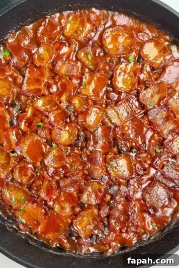 Smoked Baked Beans topped with crispy bacon in a large cast iron skillet.