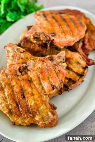 Smoked pork chops with grill marks stacked on a white platter.
