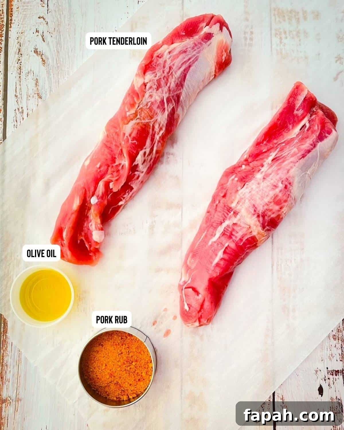 Two raw pork tenderloins on a white table with a container of olive oil and a silver container containing pork dry rub.