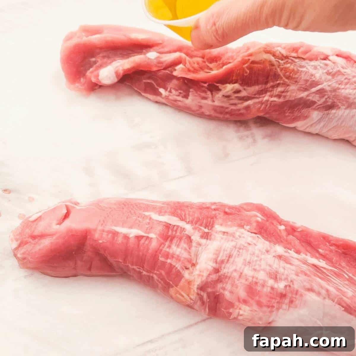 Olive oil being poured out of a small container onto the pork tenderloin.