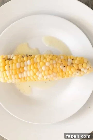 Smoked corn on the cob with melted butter and salt and pepper on a white dinner plate.
