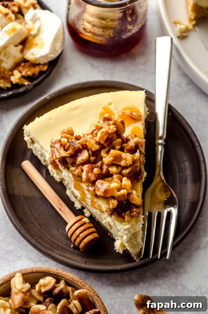 Goat Cheese Cheesecake with Roasted Honey Walnut Topping 13 A slice of goat cheese cheesecake on a plate with a honey stick and a fork.