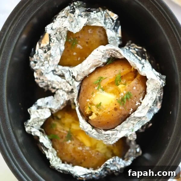 Jacket potatoes half covered in foil inside a slow cooker.