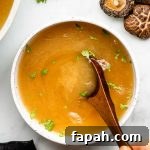 vegan bone broth in a white bowl with cilantro and spoon inside bowl