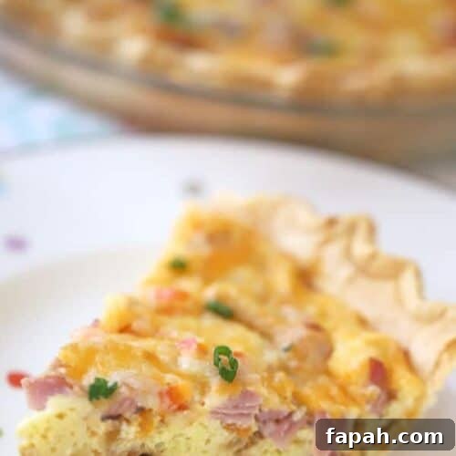 A slice of ham and cheese quiche on a white plate.