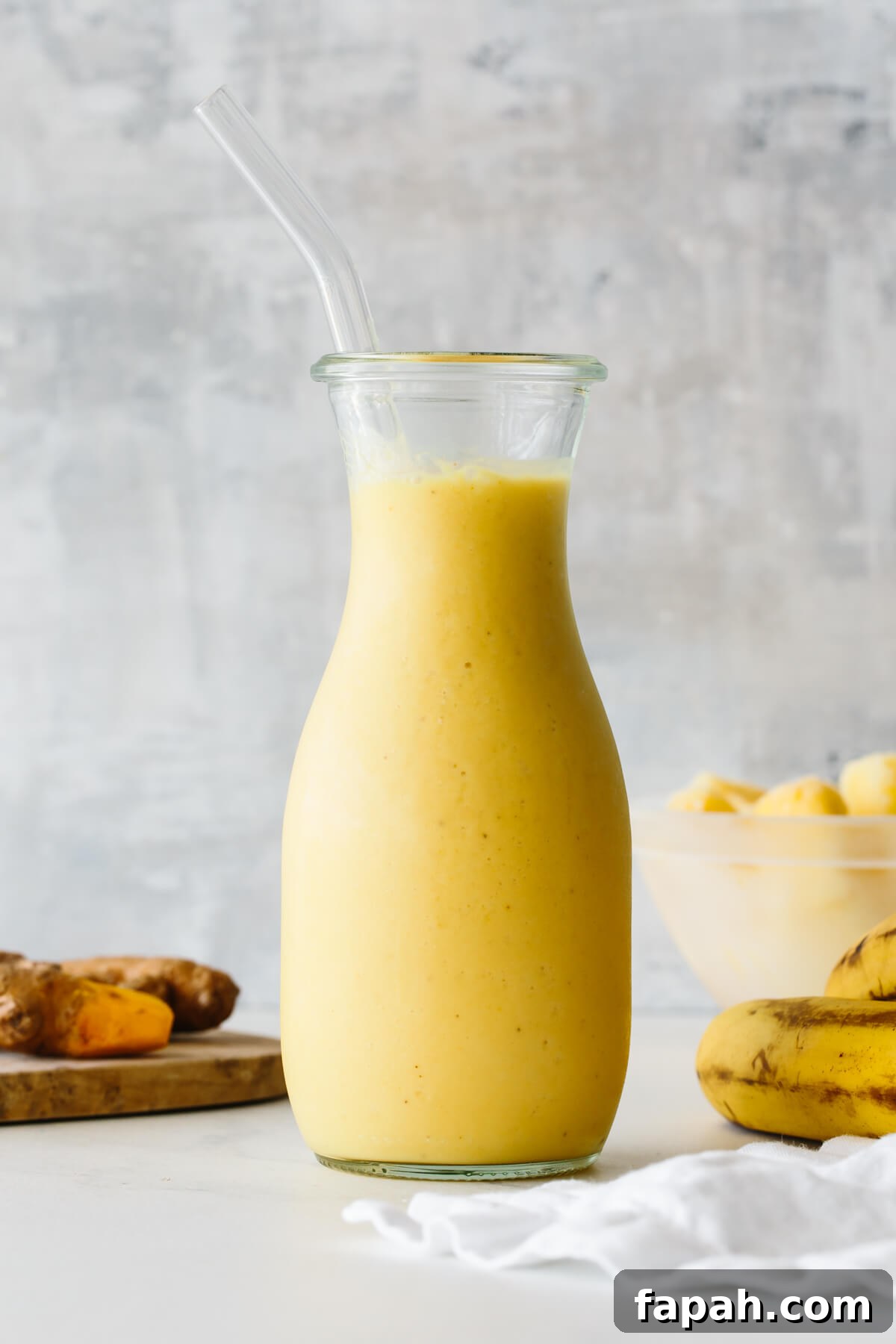 Turmeric smoothie in a glass jar with straw and ingredients in the background.