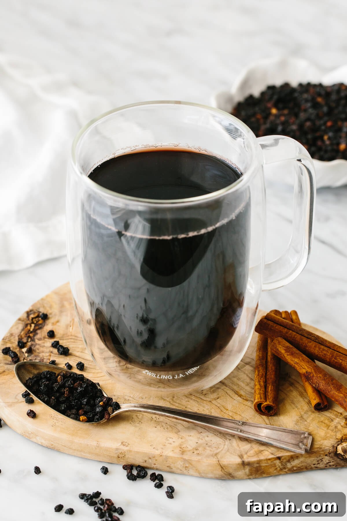 Elderberry tea in a glass next to dried elderberry and cinnamon sticks.