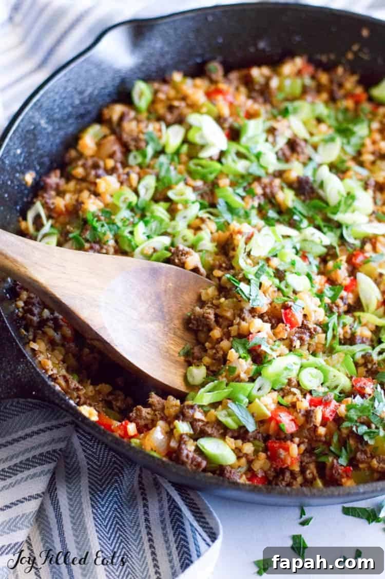 a skillet with dirty rice made from venison and cauliflower and green onions sprinkled on top