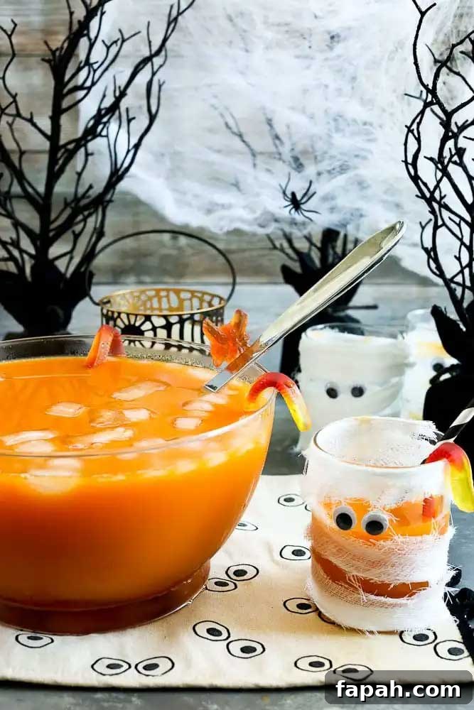 Two glasses decorated like mummies next to a clear glass punch bowl filled with non-alcoholic punch