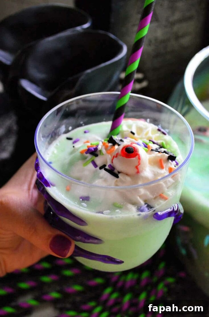 Hand holding a glass of kids' punch with Halloween sprinkles and a candy eyeball