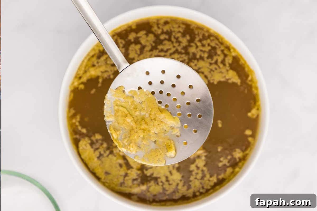 fat being skimmed off the top of broth in bowl.