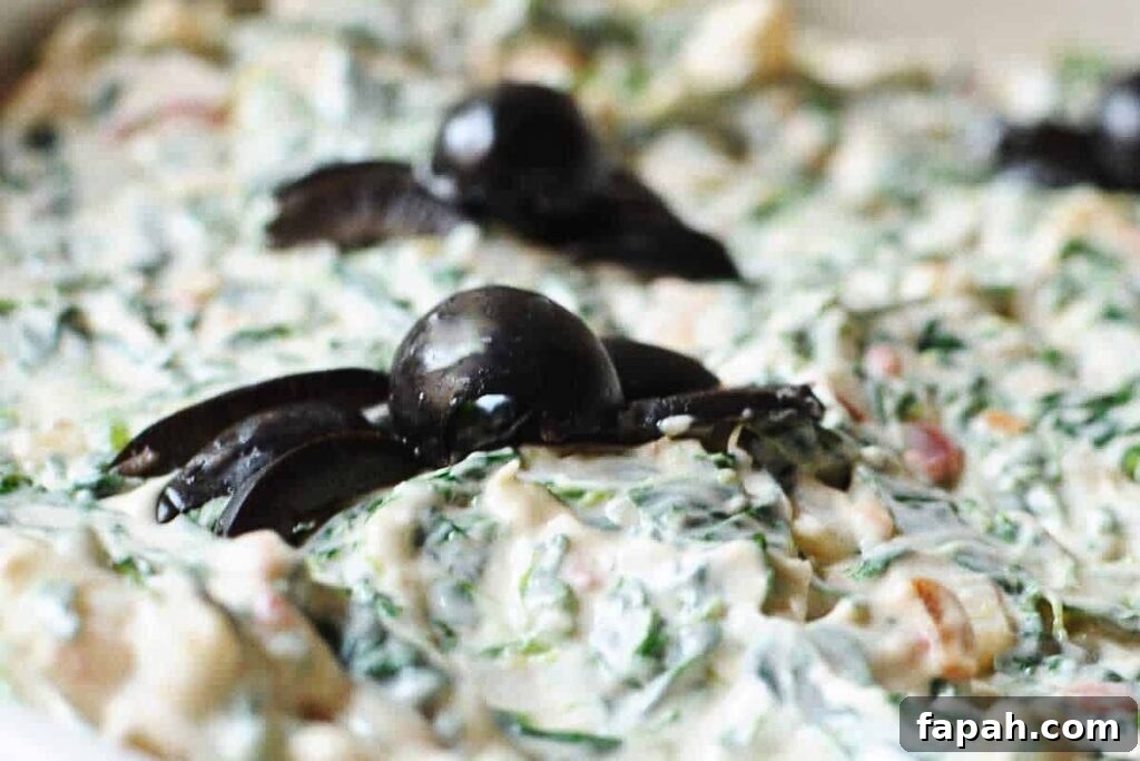 A dish of spinach dip with olive spiders.