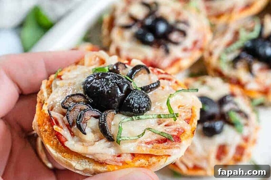 A hand holding a spider bagel bite pizza.