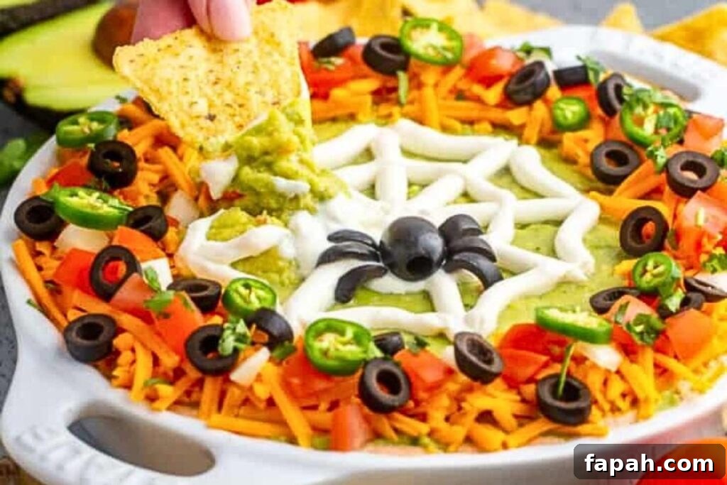 A dish of taco dip with a sour cream web and an olive spider.